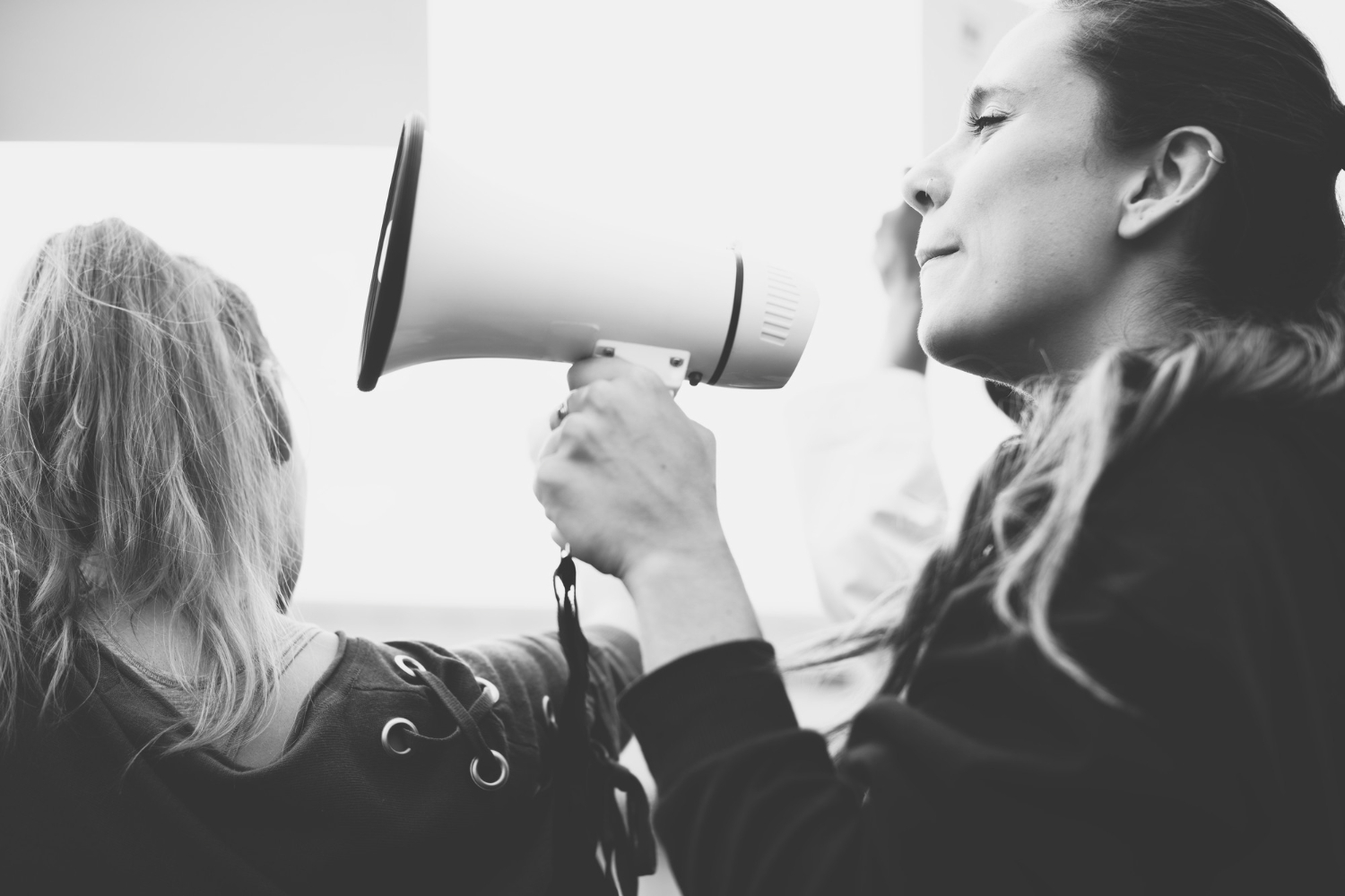 Black and white photo of a woman speaking into a megaphone beside another person, symbolising communication, voice, and advocacy