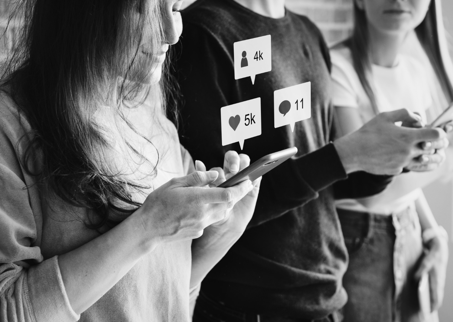A black-and-white photo of three people standing side by side, each looking at their phones. Floating social media icons above the screens display engagement metrics such as likes, comments, and followers