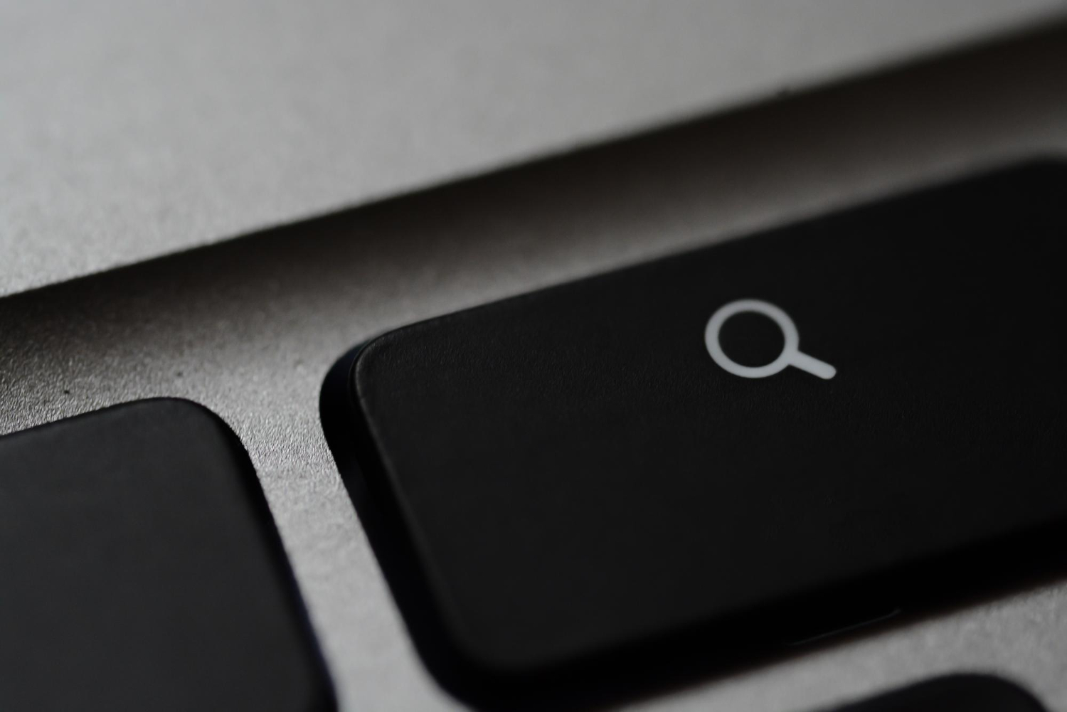 Close-up of a keyboard showing a black key with a white magnifying glass search icon.