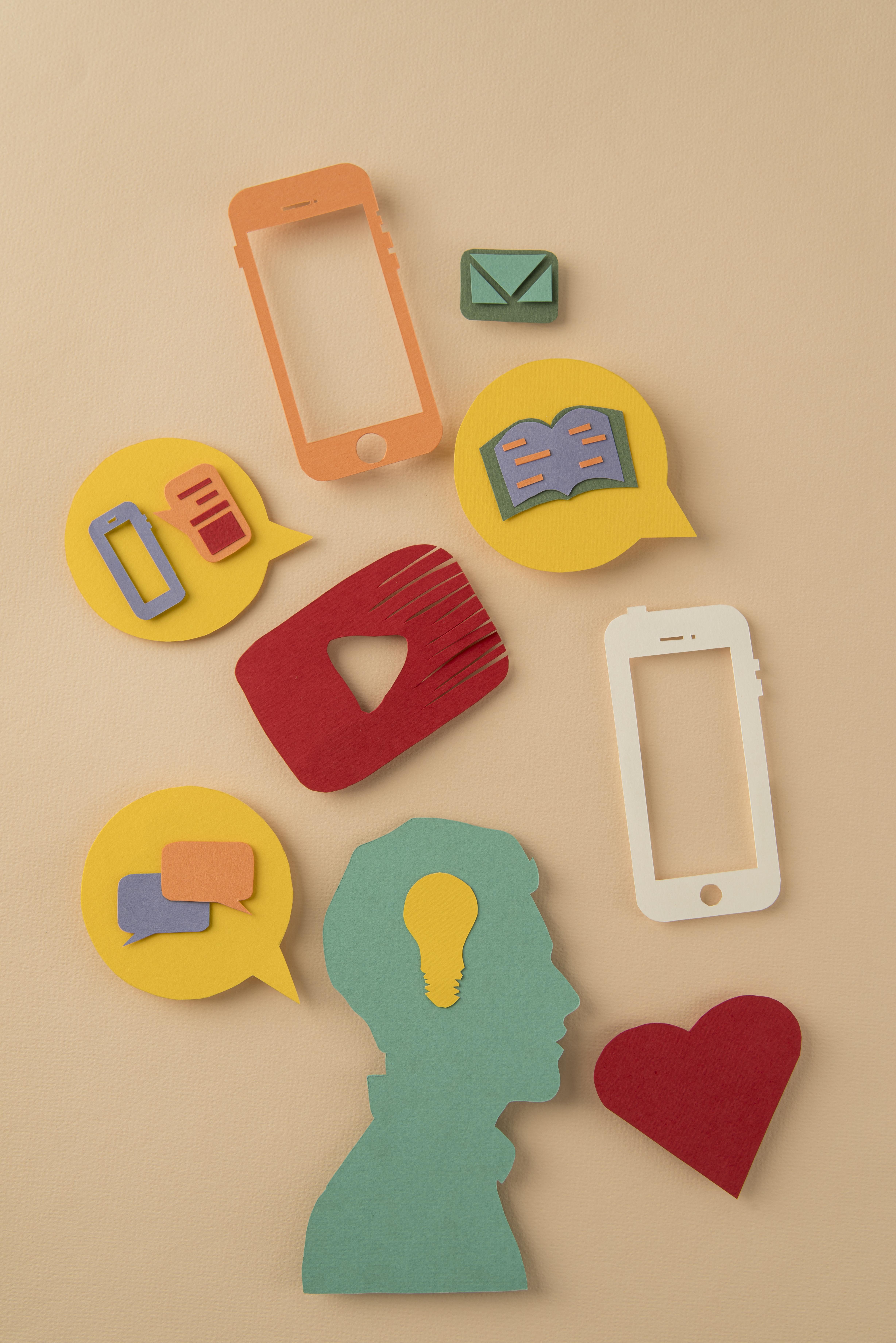 Cutout icons of social media symbols, speech bubbles, and mobile phones arranged above a silhouette of a person’s head on a beige background.